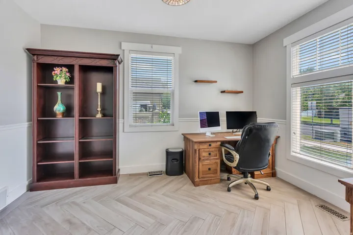 Versatile room featuring light wood-finish flooring in a herringbone pattern, a large window with white blinds, and white wainscoting