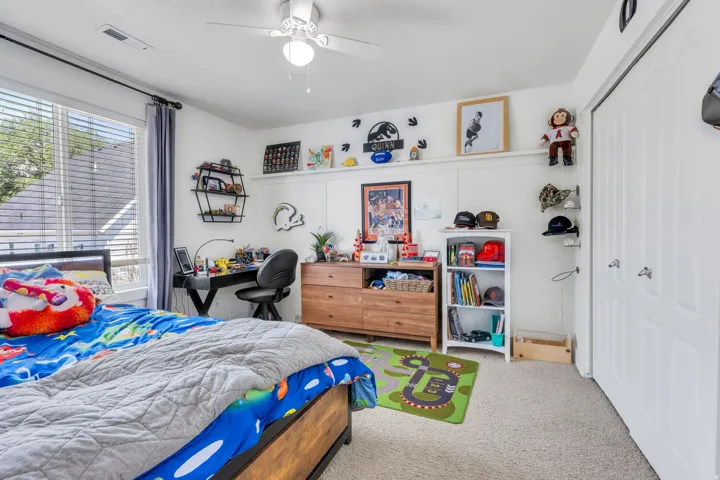 Bedroom featuring a large window with blinds, ceiling fan, carpet flooring, a built-in desk area, and a closet with bifold doors