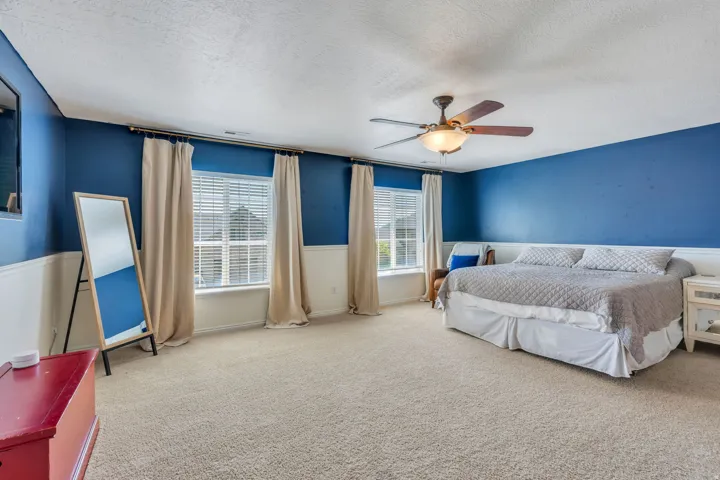 Spacious bedroom with bold blue accent walls, ceiling fan with integrated lighting, and neutral carpet flooring
