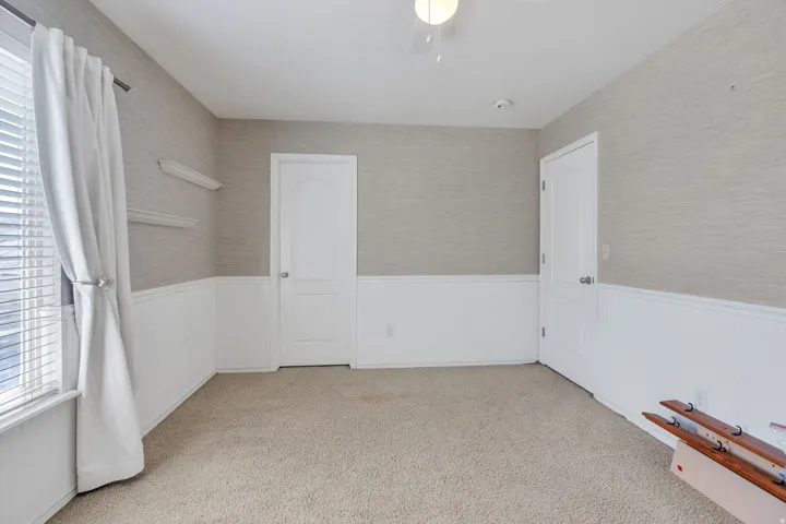 Carpeted room featuring wainscoting, textured wallpaper, and two paneled doors with chrome hardware
