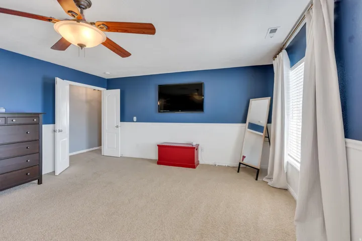 Spacious interior featuring neutral carpet flooring, a ceiling fan with integrated lighting, and a wall-mounted television