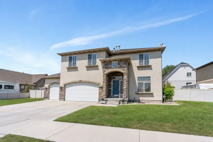 Two-story stucco residence featuring a stone facade accent, arched entryway, and multiple garage bays