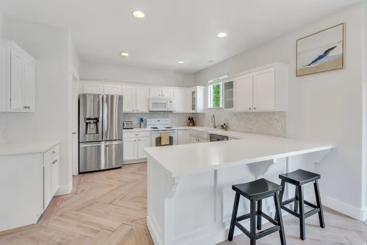 Kitchen featuring a U-shaped countertop with seating, white shaker-style cabinetry, stainless steel appliances, and a herringbone-patterned wood-finish floor