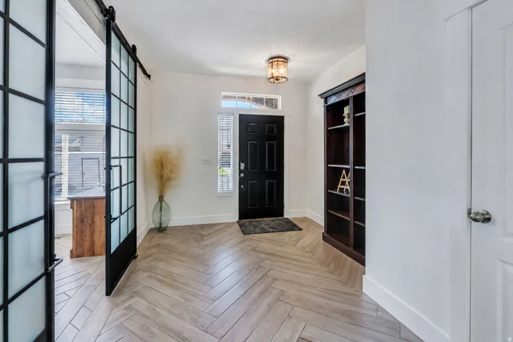 Entryway featuring herringbone-pattern wood-finish flooring, a dark-paneled door with a transom window, and a built-in dark wood bookcase