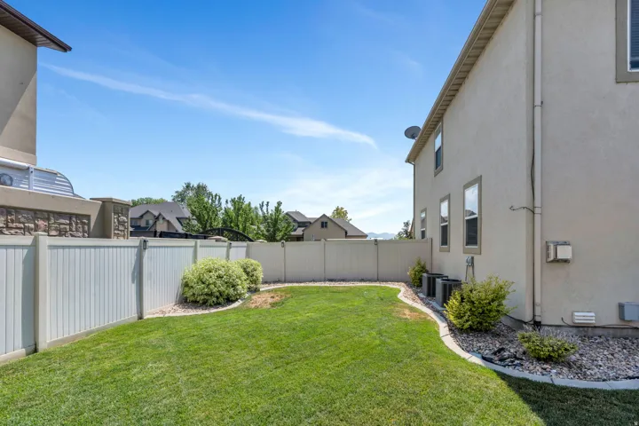 Expansive backyard featuring a manicured lawn, white privacy fencing, and decorative gravel landscaping with shrubs