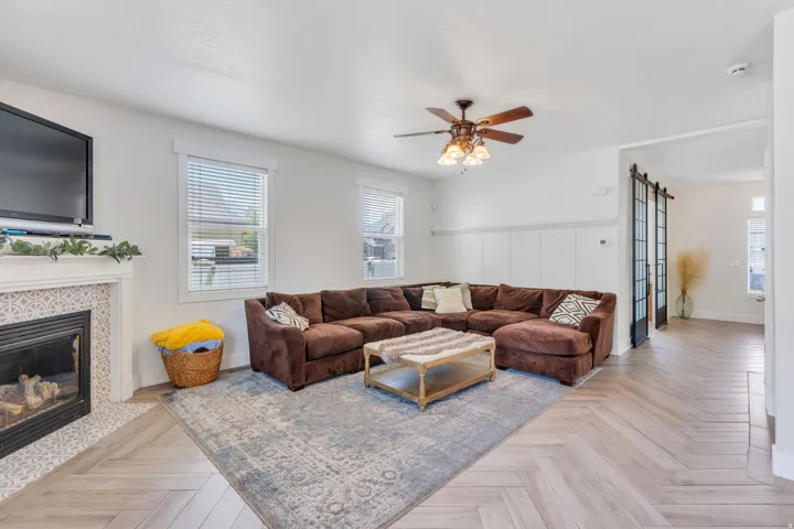 Living area featuring chevron pattern wood-finish flooring, a fireplace with decorative tile surround and mantel, and white wainscoting
