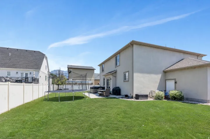 Expansive rear yard featuring a manicured lawn, concrete patio, and stucco exterior