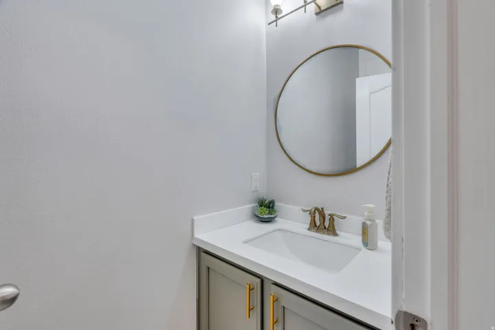 Vanity area featuring a round brass-framed mirror, dual-handle brass-tone faucet, integrated sink, and white countertop