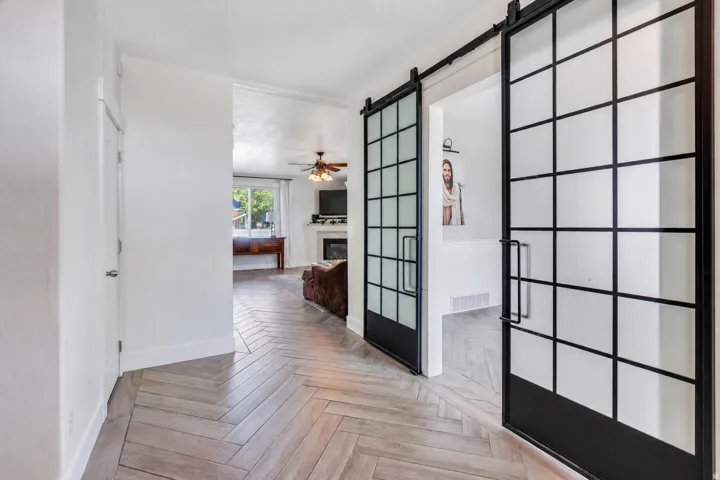 Herringbone wood-finish flooring enhances this entryway, featuring two frosted-paneled barn doors with black hardware