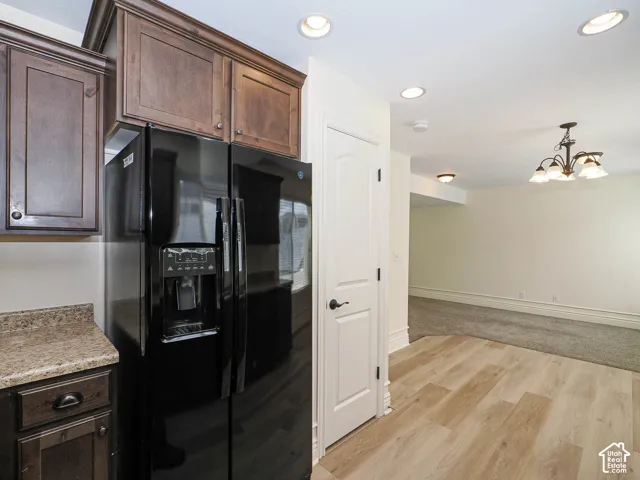 Dark wood-finish cabinetry, black side-by-side refrigerator, speckled countertop, wood-finish flooring, and recessed lighting