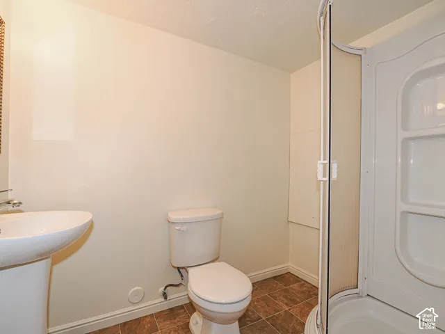 Functional bathroom featuring a pedestal sink with chrome fixtures, an enclosed shower stall with glass enclosure, and ceramic tile flooring