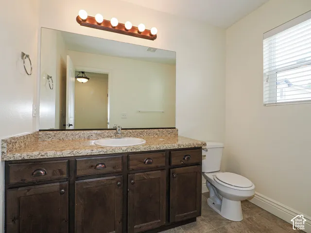 Bathroom featuring a wood-finish vanity with an integrated sink, a speckled countertop, a large wall-mounted mirror, and a window with blinds