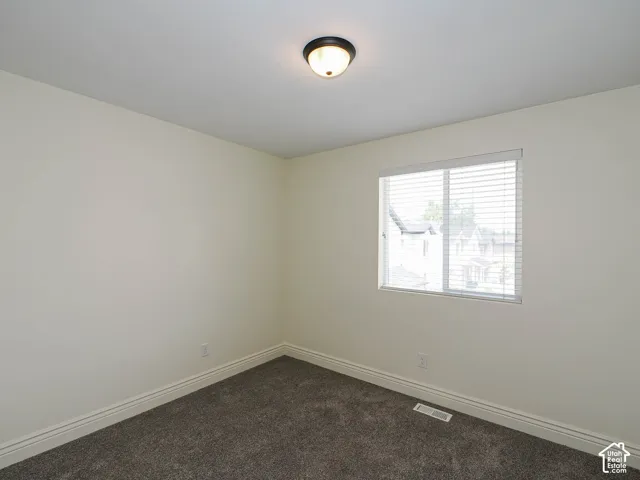 Plush carpet flooring, neutral wall tones, window with horizontal blinds, and a flush-mount ceiling light fixture