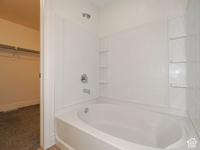 White porcelain bathtub with integrated shower, chrome fixtures, and built-in shelving