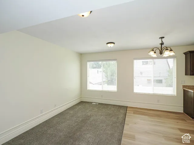 Two large windows with blinds, dual flooring featuring carpet and wood-finish, and a bronze chandelier