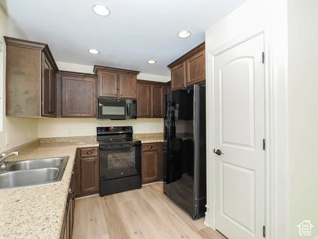 Kitchen featuring wood-finish flooring, dark wood cabinetry, light speckled countertops, and integrated black appliances