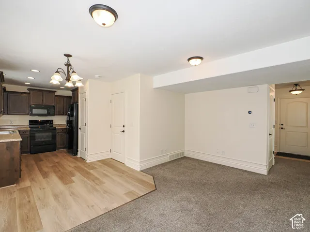 Open-concept living space with wood-finish flooring, dark wood cabinetry, black appliances, and neutral carpet