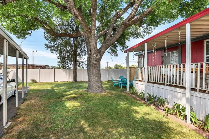 Spacious backyard featuring a mature shade tree, level lawn, and covered porch with red metal roof and white railings