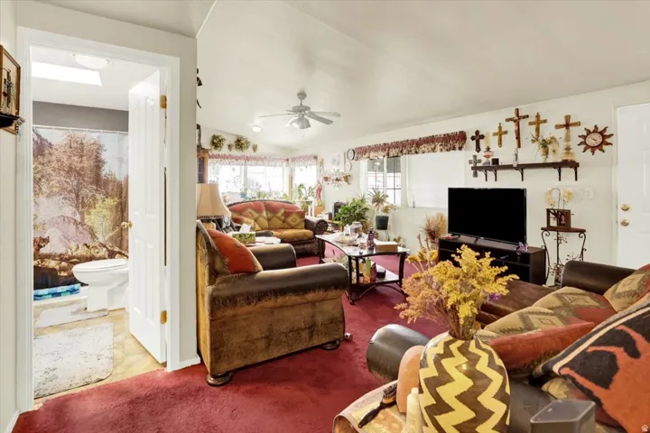 Spacious living area featuring red carpeting, white walls, and a ceiling fan