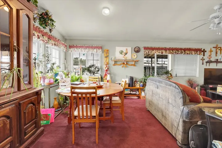 Spacious living area featuring hardwood dining table with matching chairs, burgundy carpeting, and abundant natural light from multiple windows