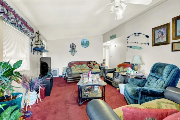 Spacious living area featuring multiple seating zones with a red carpet foundation, ceiling fan for air circulation, and abundant natural light from windows with blinds