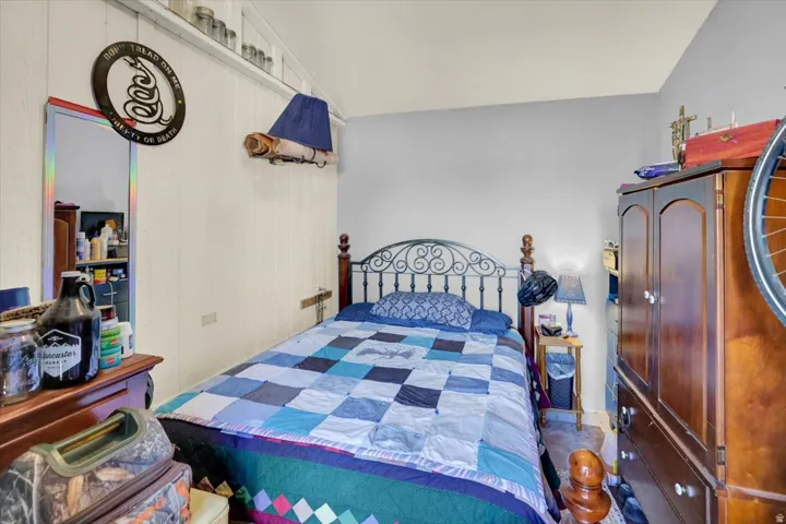 Bedroom featuring a decorative metal bed frame with blue upholstered headboard, patchwork quilt bedding in blue and purple tones, wood-finish flooring, and wood cabinetry