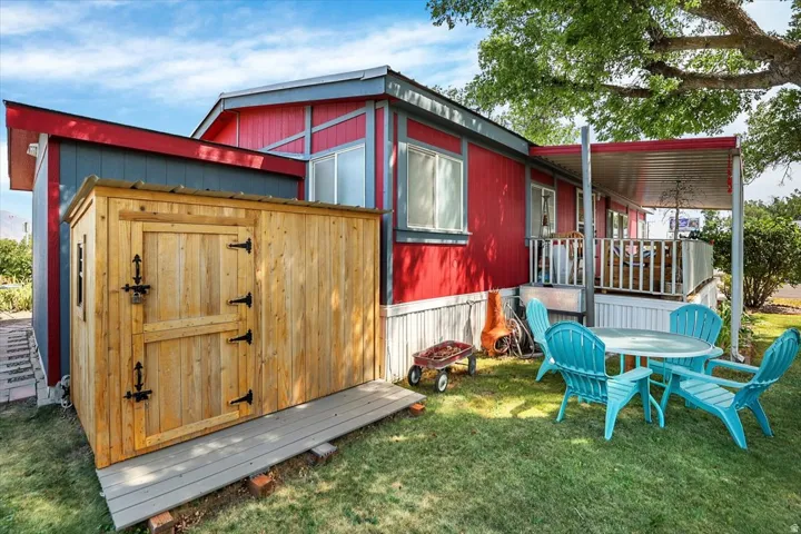 Red-sided dwelling featuring a covered porch, a separate storage shed, a sloped roofline, and a grassy outdoor area