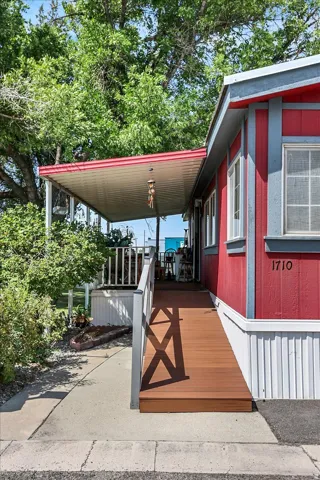 Charming red manufactured home featuring a covered front porch with metal railings and wood-finish decking