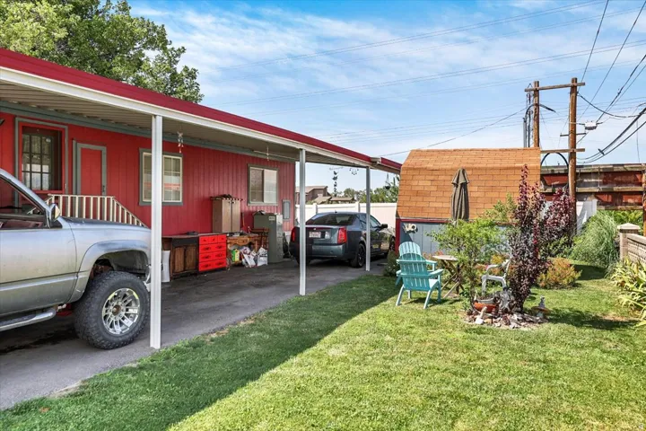 Red-sided structure featuring a covered carport and a secondary shed with a gambrel roof