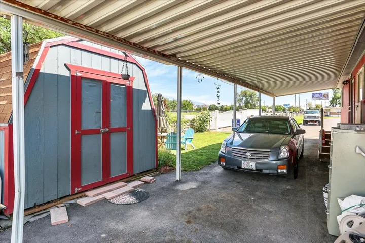 Covered carport with ample parking space, featuring a detached storage shed with red-trimmed doors and gray siding