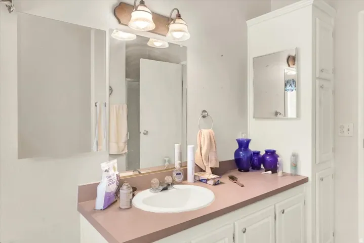 Bathroom vanity featuring a single basin sink, a large wall-mounted mirror, and overhead sconce lighting