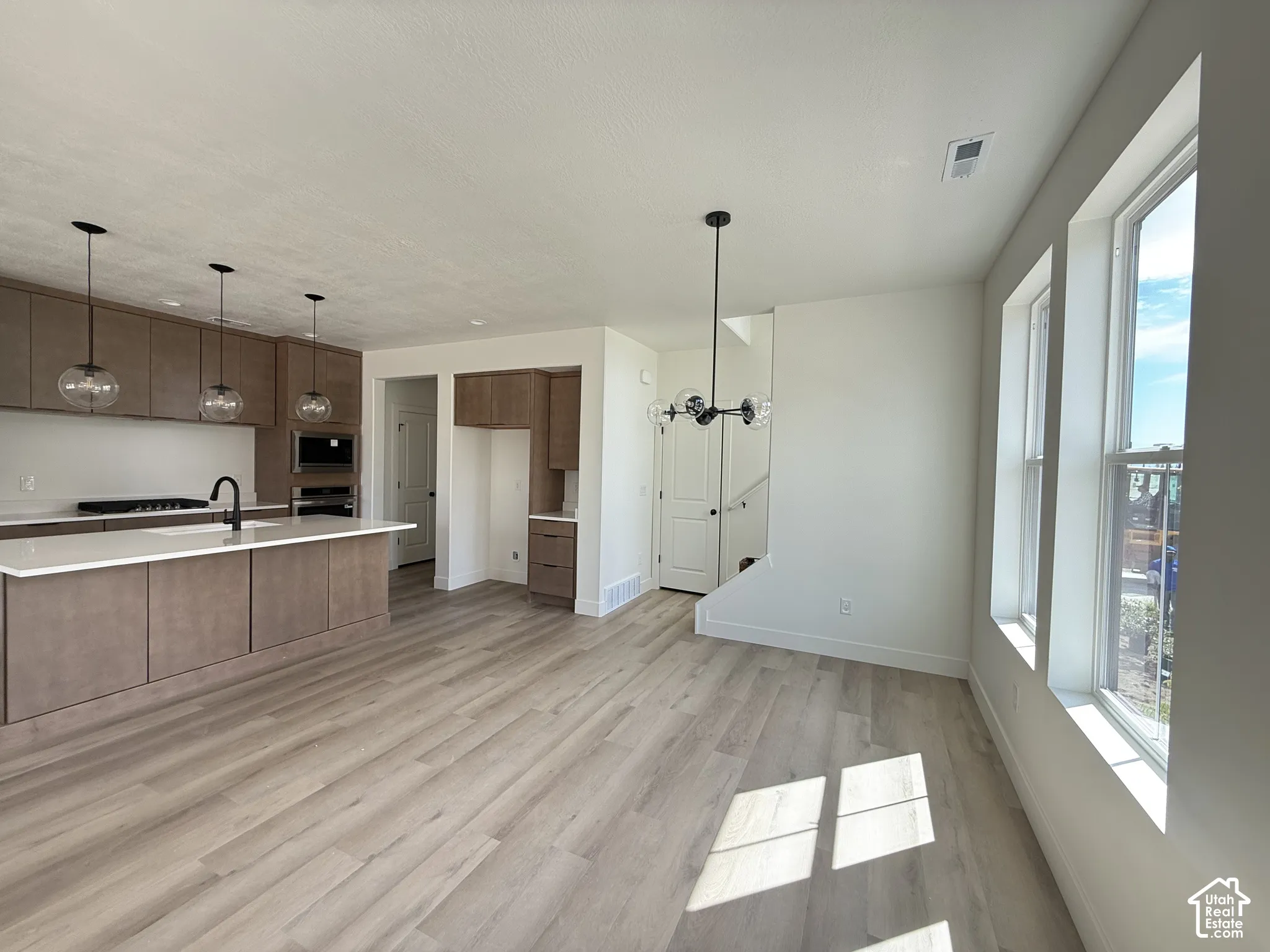 Wood-finish flooring, contemporary kitchen island with white countertop, integrated appliances, modern pendant lighting, and multiple windows