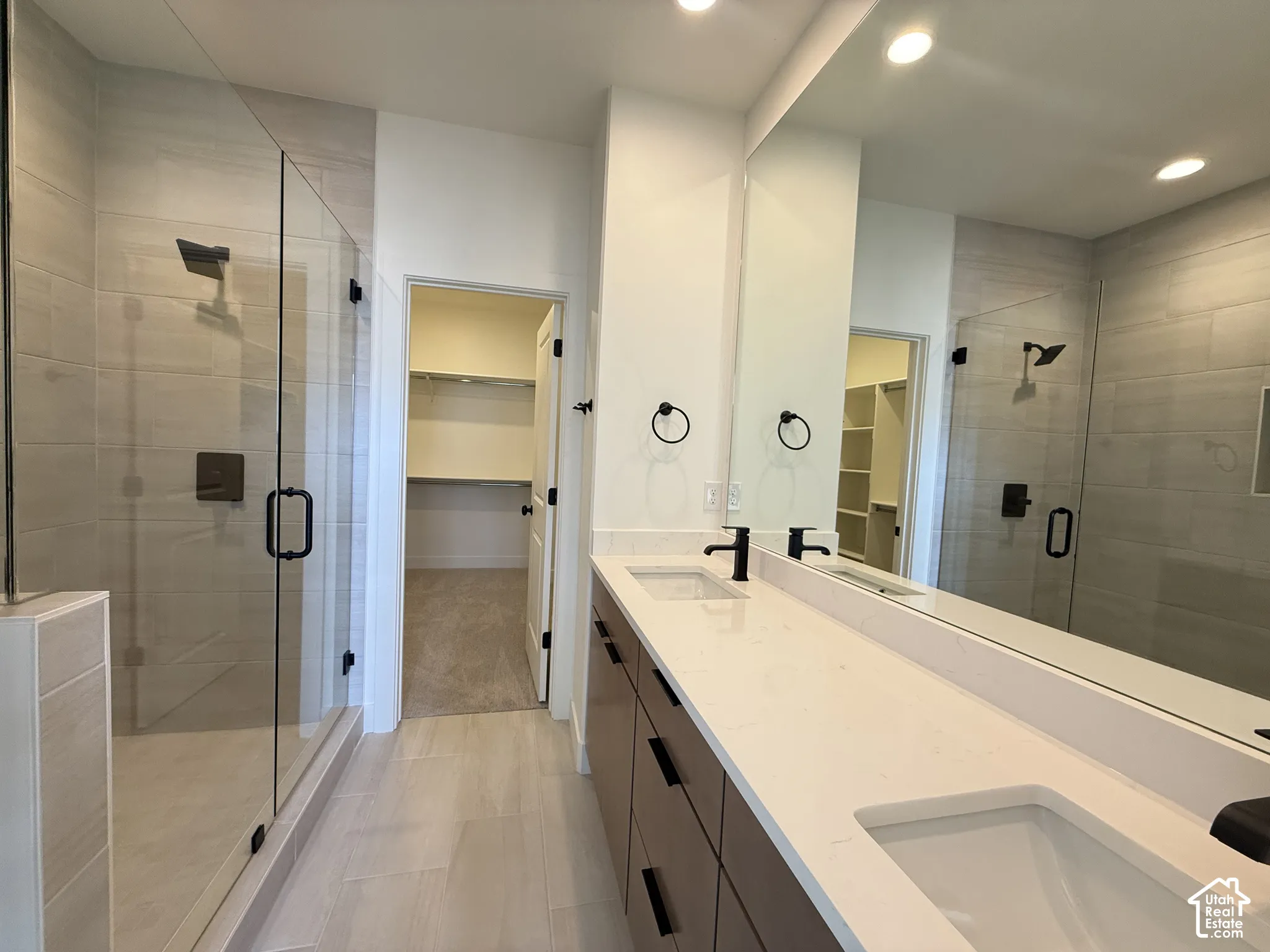 Dual vanity with integrated sinks, expansive mirror, walk-in shower with glass enclosure, built-in shelving, and wood-finish flooring