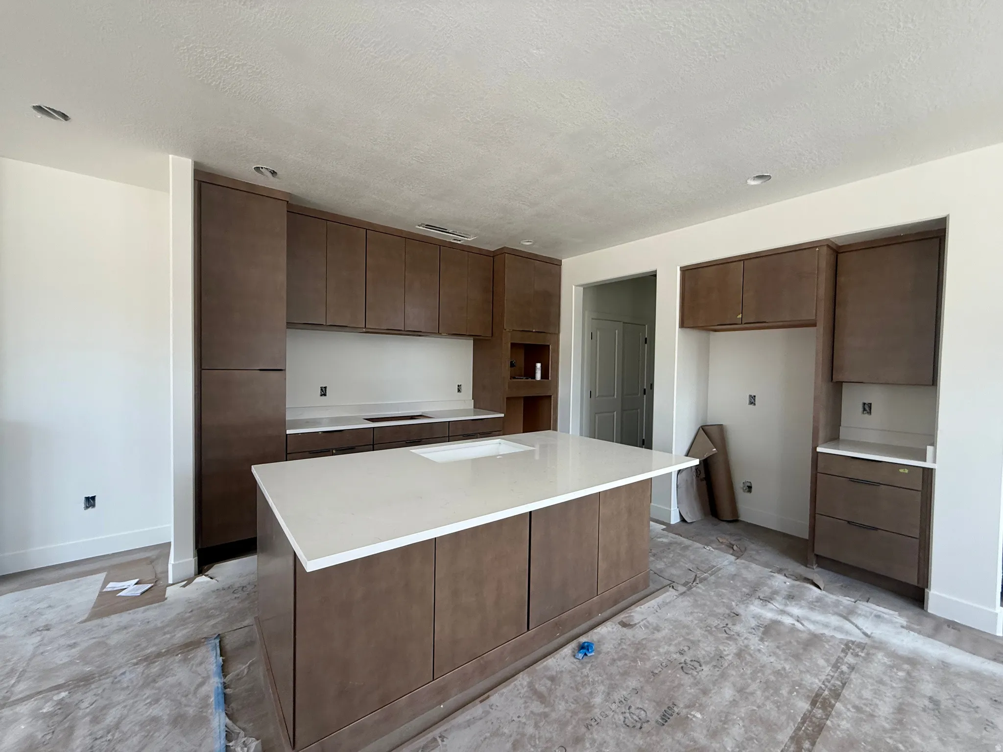 Kitchen featuring a central island with an integrated sink, light-toned countertops, contemporary flat-panel cabinetry, and recessed lighting