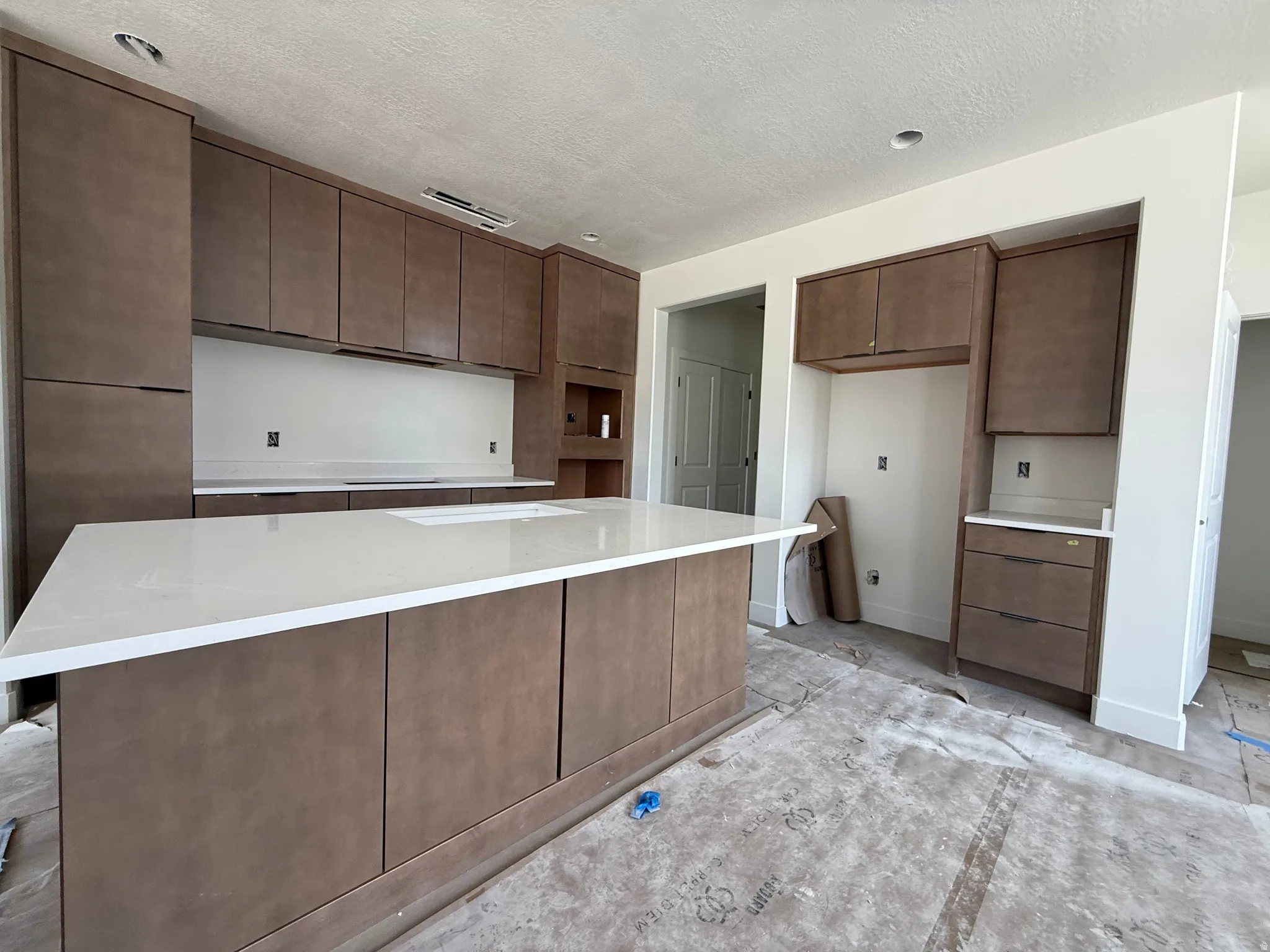Kitchen featuring a large central island with a built-in sink and light-toned countertops, extensive cabinetry with dark hardware, recessed lighting, and white walls