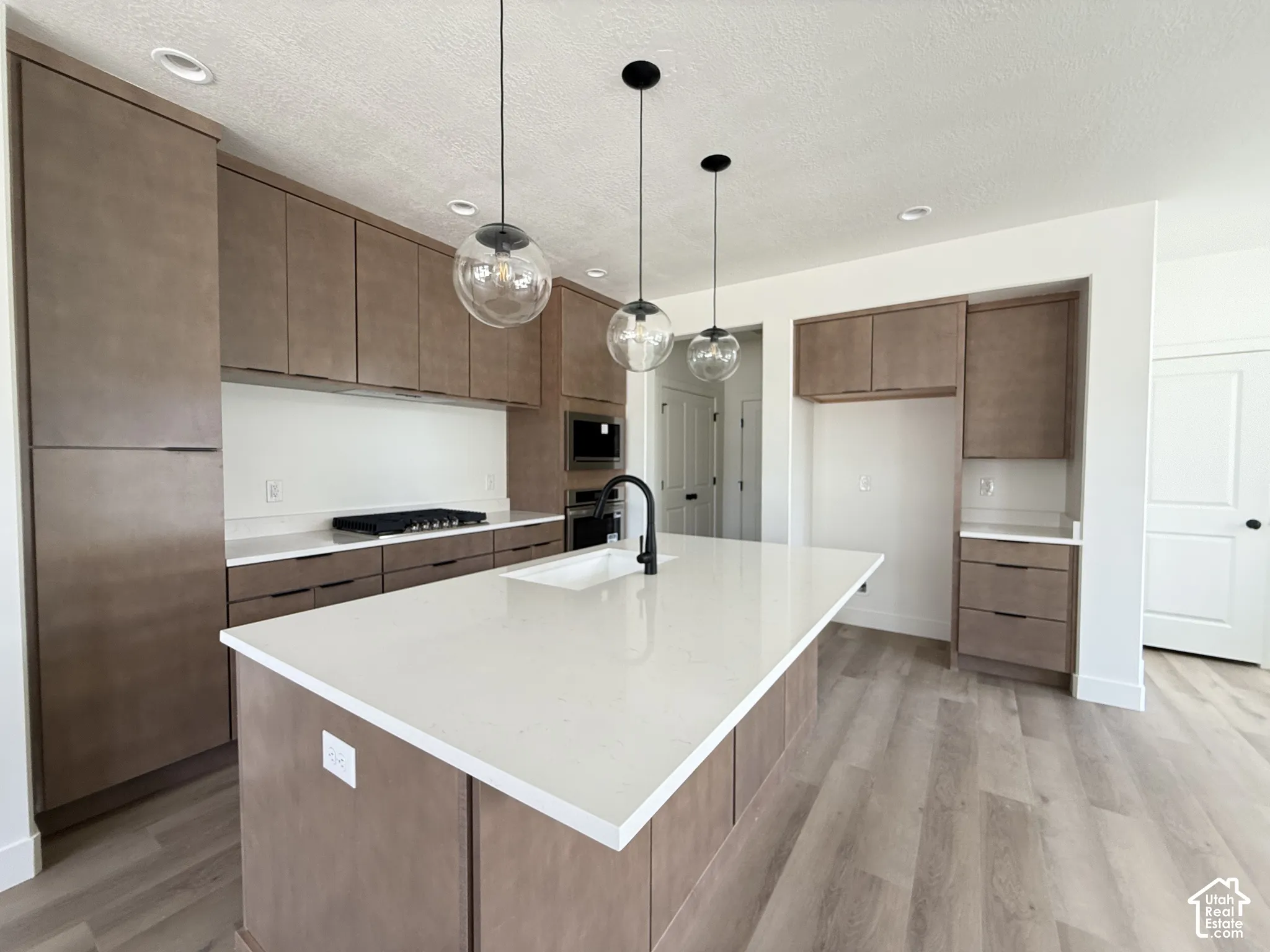 Modern kitchen with wood-finish cabinetry, white countertops, and a central island with an integrated sink