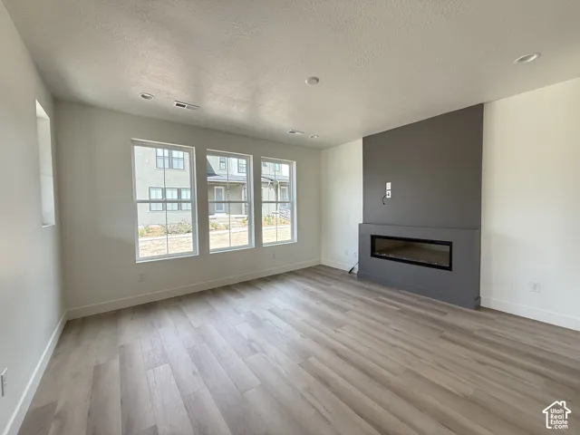 Wood-finish flooring, recessed lighting, multiple windows, and a built-in linear fireplace with a textured accent wall