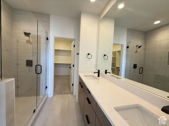 Dual vanity with integrated sinks, expansive mirror, walk-in shower with glass enclosure, built-in shelving, and wood-finish flooring