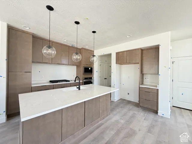 Contemporary kitchen featuring wood-finish cabinetry, light-toned countertops, a center island with an integrated sink, and pendant lighting fixtures