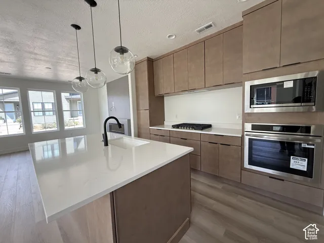 Kitchen featuring an integrated wall oven, microwave, gas cooktop, and a large central island with an undermount sink and matte black faucet