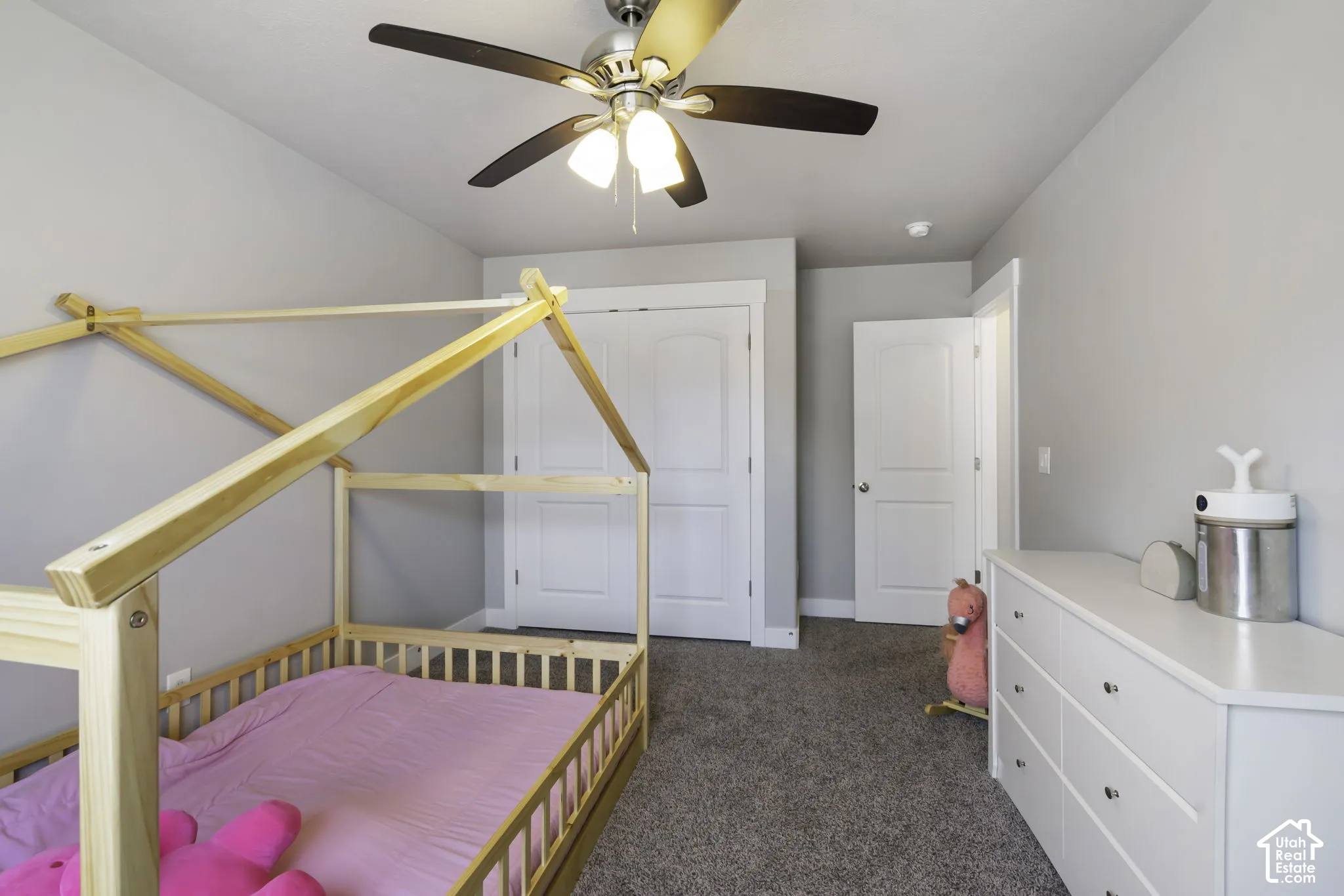 Carpeted room featuring a ceiling fan with integrated lighting, a white six-drawer dresser with silver hardware, and white interior doors with matching hardware