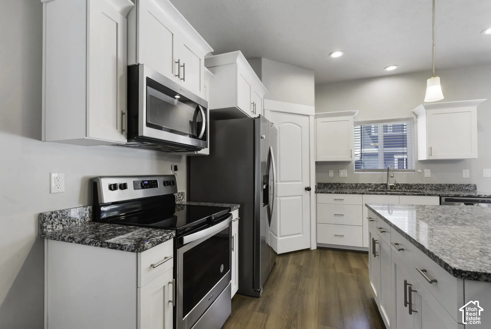 Modern kitchen featuring white cabinetry, granite countertops, stainless steel appliances, wood-finish flooring, and recessed lighting