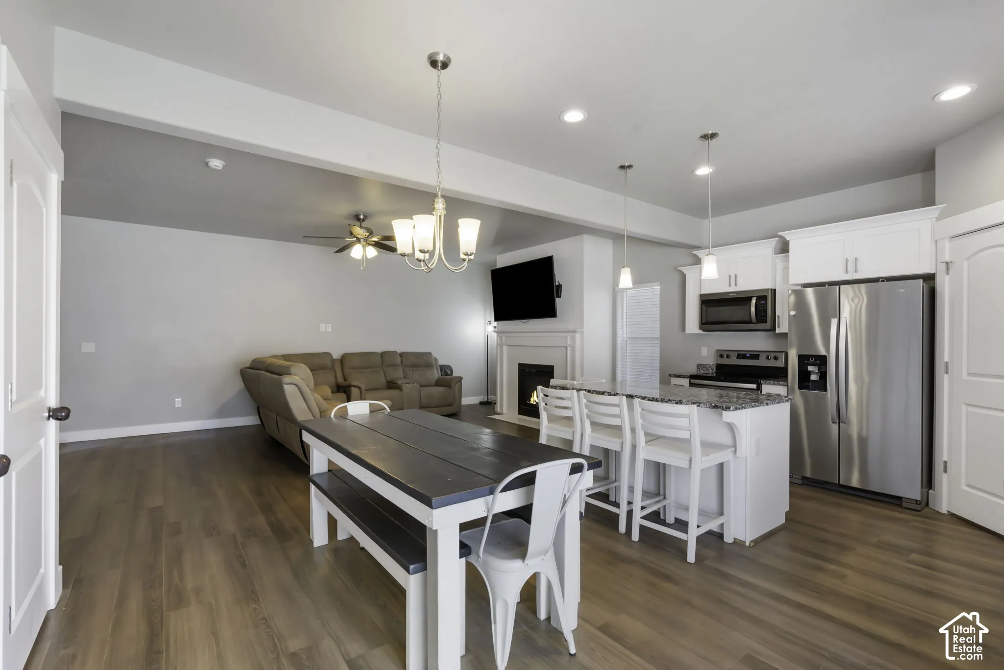 Open-concept living space featuring wood-finish flooring, a kitchen island with seating, stainless steel appliances, white cabinetry, and a fireplace