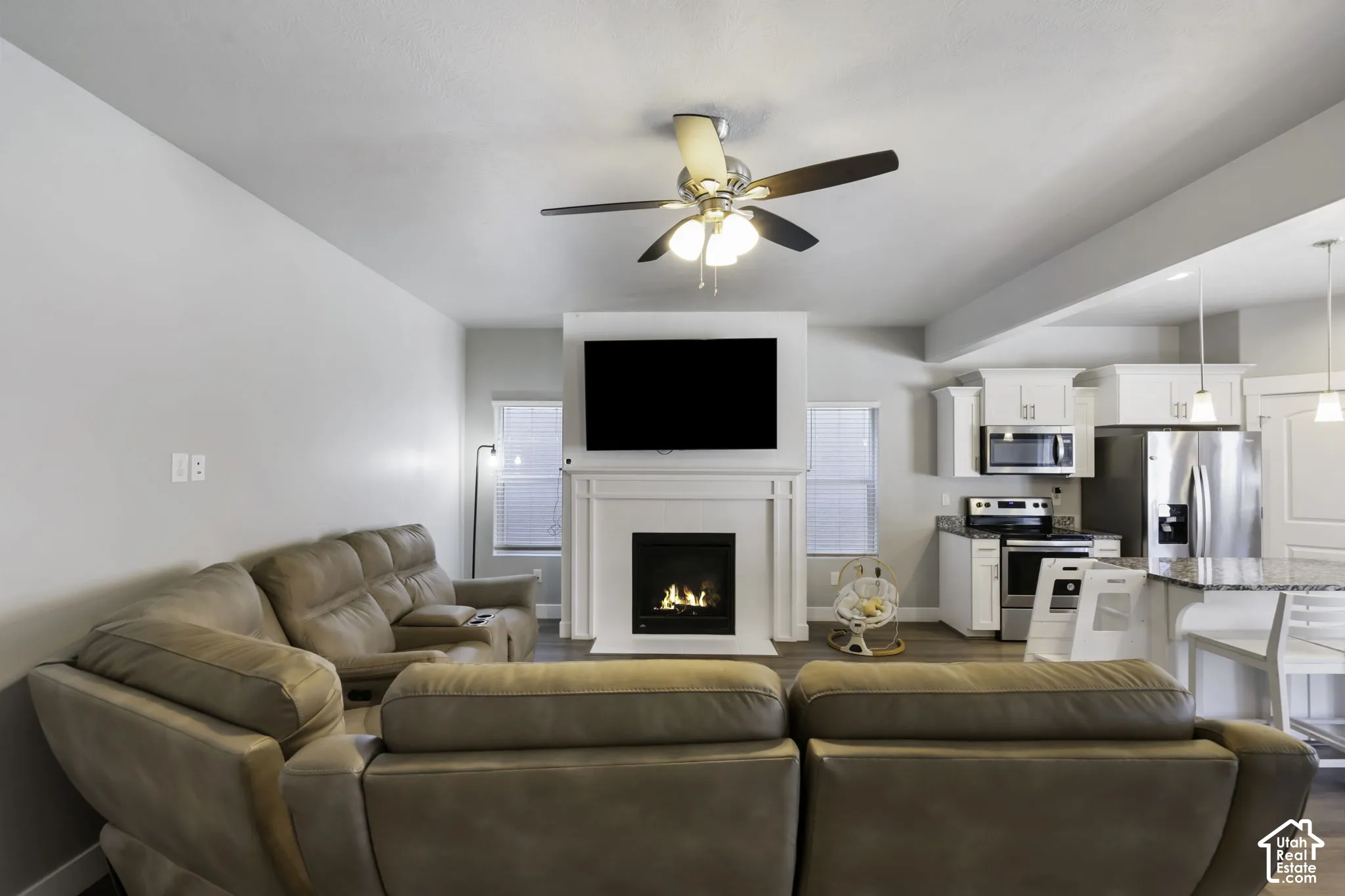 Living area featuring a gas fireplace with a white mantel, ceiling fan, and wood-finish flooring