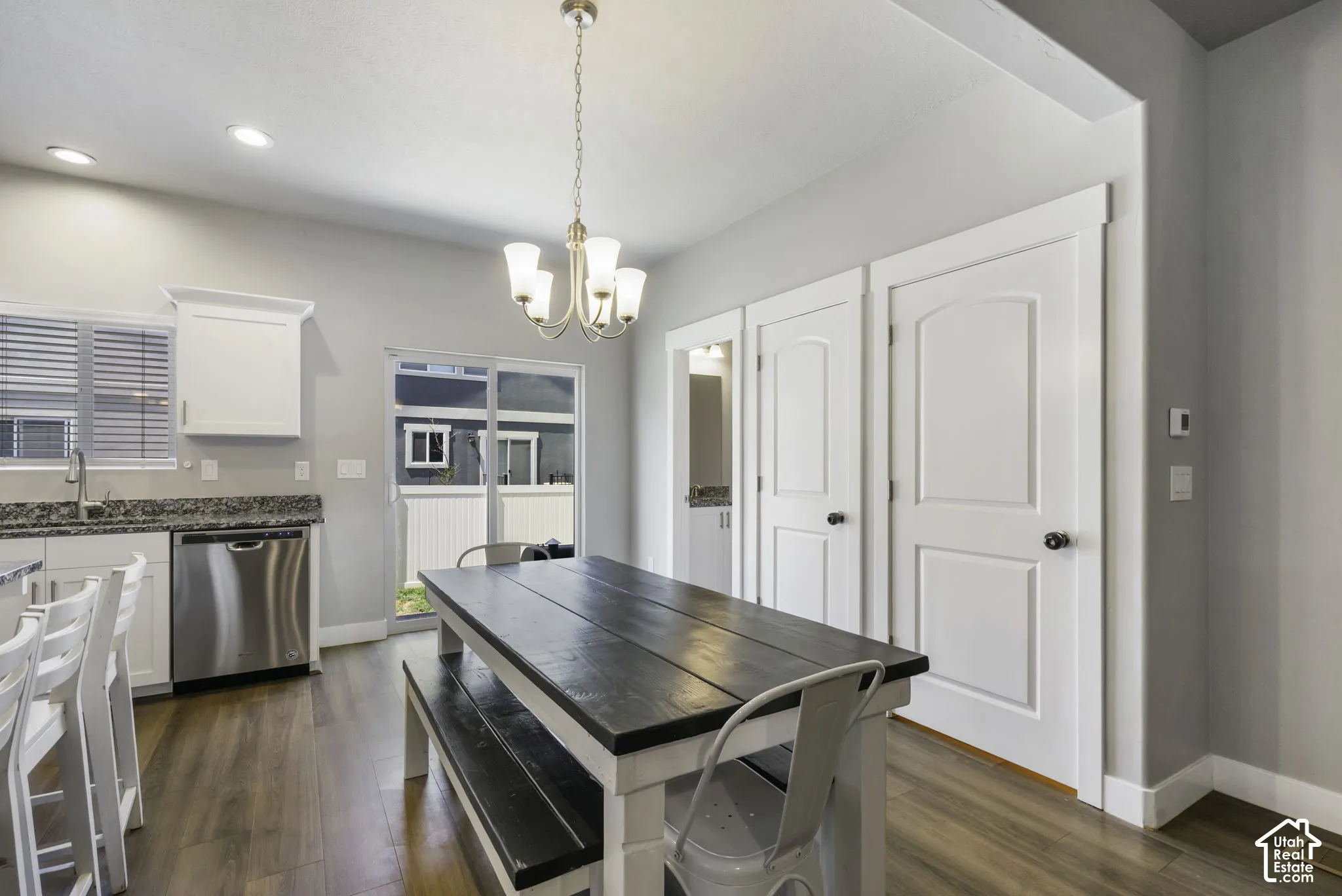 Kitchen and dining area featuring wood-finish flooring, white cabinetry, stainless steel dishwasher, speckled countertops, and a sliding glass door