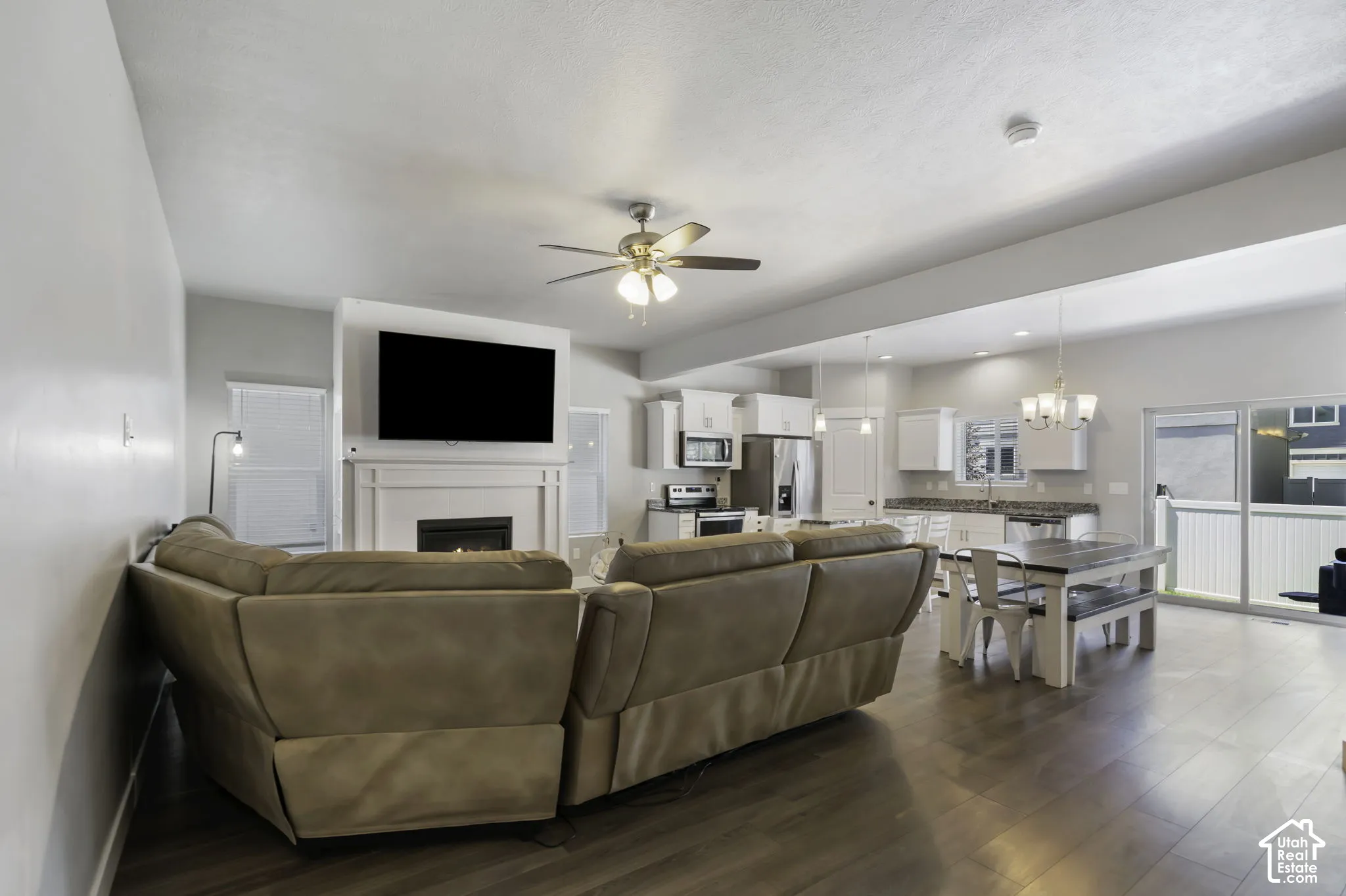 Open-concept living space featuring wood-finish flooring, a ceiling fan with integrated lighting, and a fireplace with a mantel