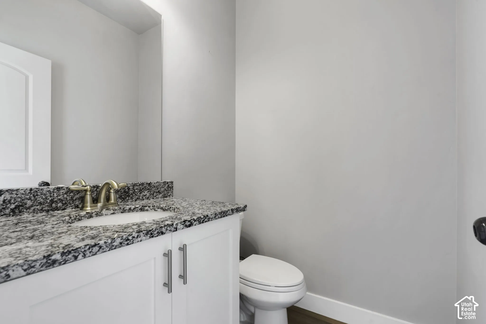 Half Bathroom vanity with a granite countertop, undermount sink, and brushed brass faucet