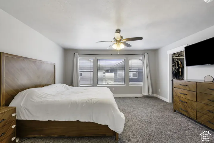 Carpeted room featuring a ceiling fan with integrated lighting, a triple window assembly with blinds, a built-in closet, and light gray wall paint