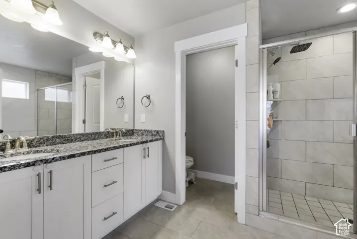 Bathroom featuring a dual vanity with a patterned countertop and white cabinetry, a large frameless mirror, and a tiled shower enclosure with a glass door