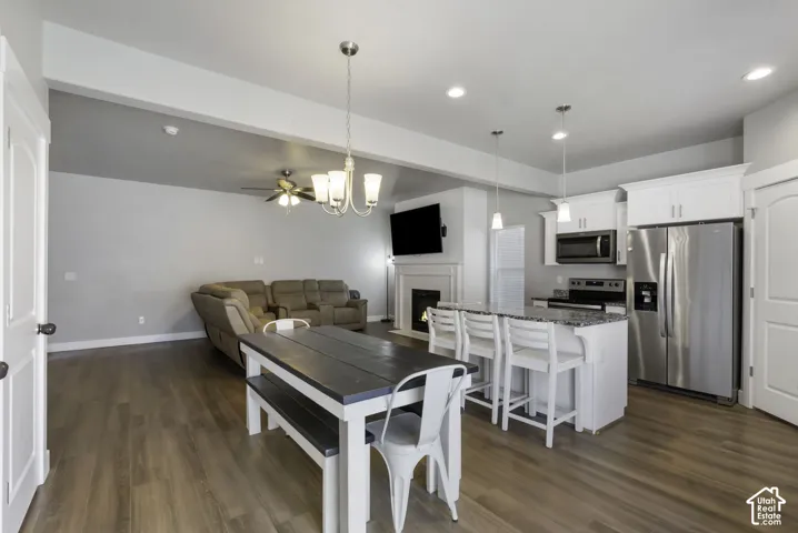 Open-concept living space featuring wood-finish flooring, a kitchen island with seating, stainless steel appliances, white cabinetry, and a fireplace
